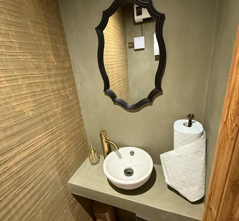 Rustic modern bathroom featuring a white vessel sink, gold faucet, and ornate black mirror.