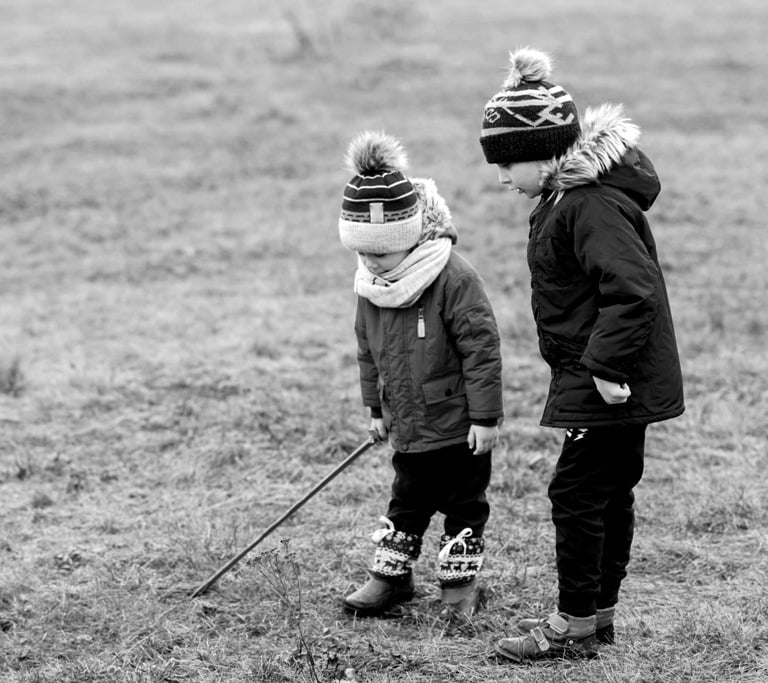 Dzieci bawią się na trawie. Chłopiec trzyma w ręku długi kijek, która imituje białą laskę.