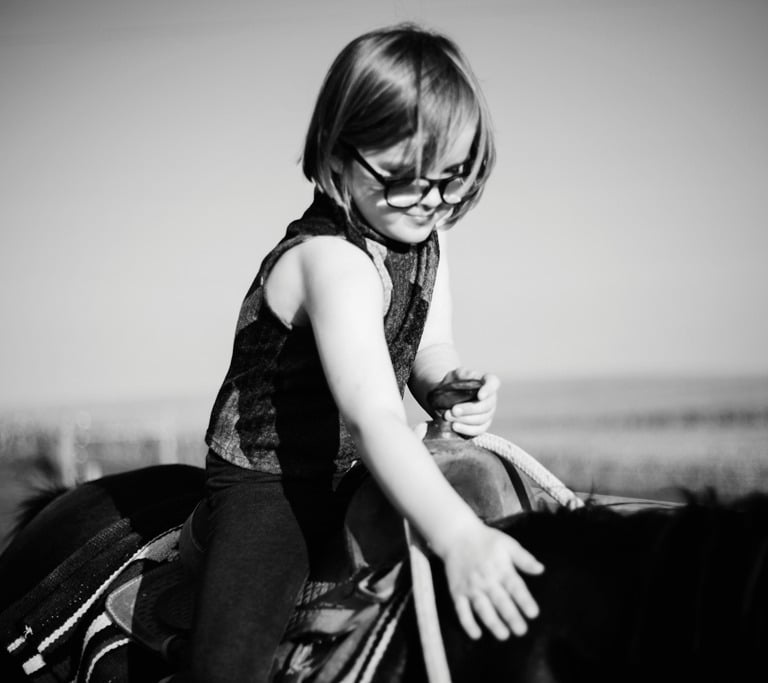 Dziewczynka w okularach siedzi na kucu. Dłonią dotyka jego grzywy.