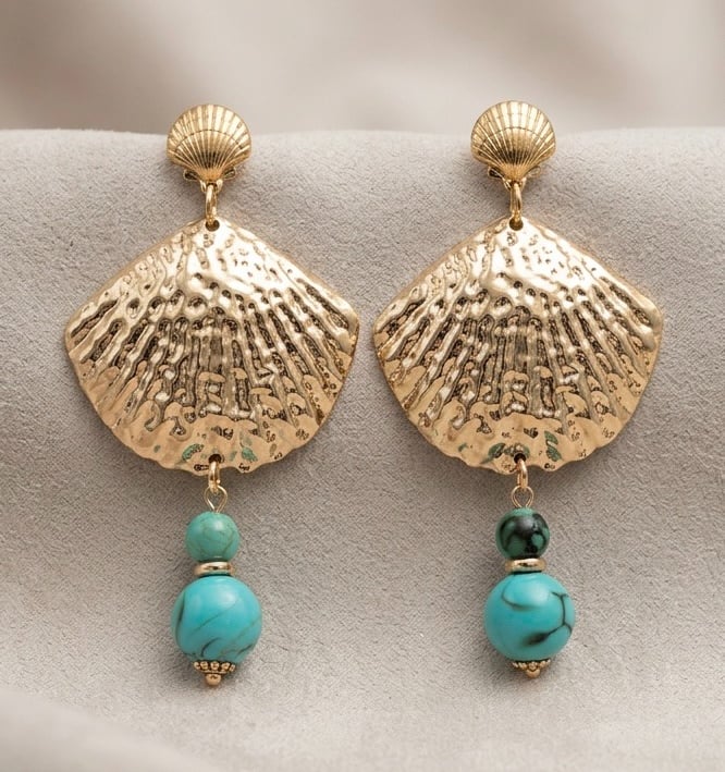 Gold seashell drop earrings with turquoise beads hanging on a neutral textured background.