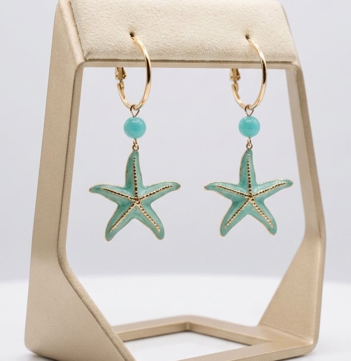 Gold hoop earrings with turquoise beads and enamel starfish charms on a jewelry display stand.