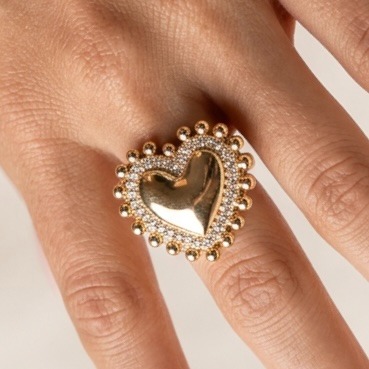 A gold heart ring with crystal accents on a woman's finger, highlighting elegant statement jewelry.