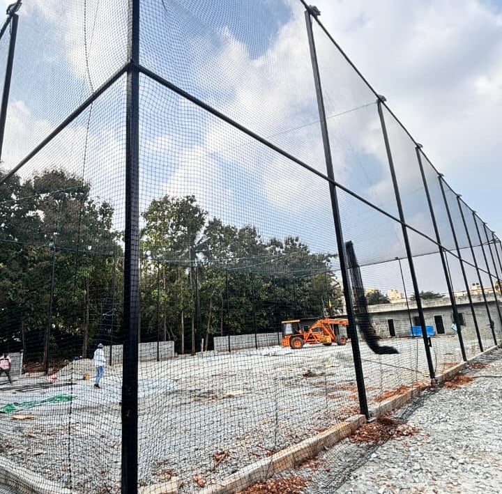 Evening view of a cricket net setup with city lights twinkling in the background.
