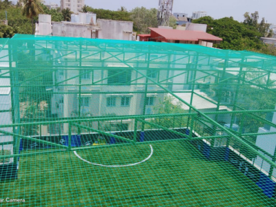 Evening view of a cricket net setup with city lights twinkling in the background.