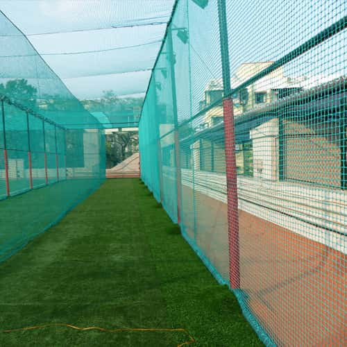 A sturdy cricket net installed on a sunny Mumbai terrace with a player practicing shots.