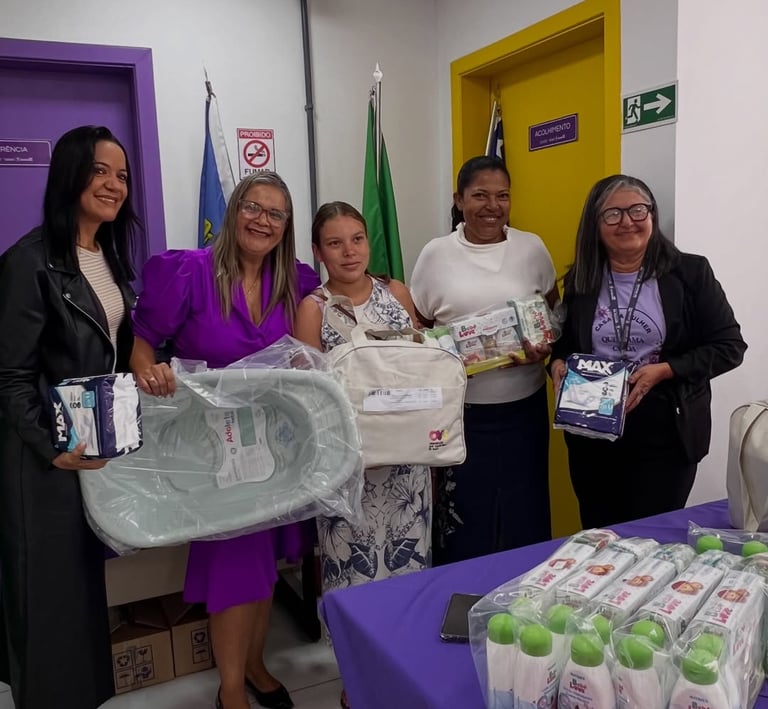 Five women holding newborn baby kits with diapers and a bathtub for maternity donation.