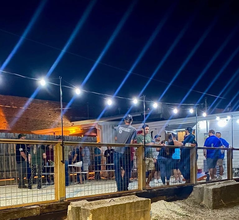 Crowd of people enjoying an outdoor nightlife event with string lights and blue stage beams.