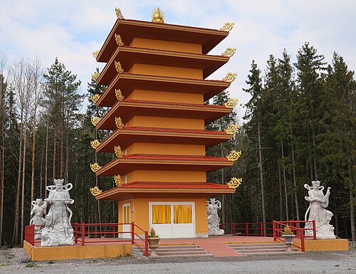 A seven-story orange Buddhist pagoda with gold accents and stone statues in a forest setting.