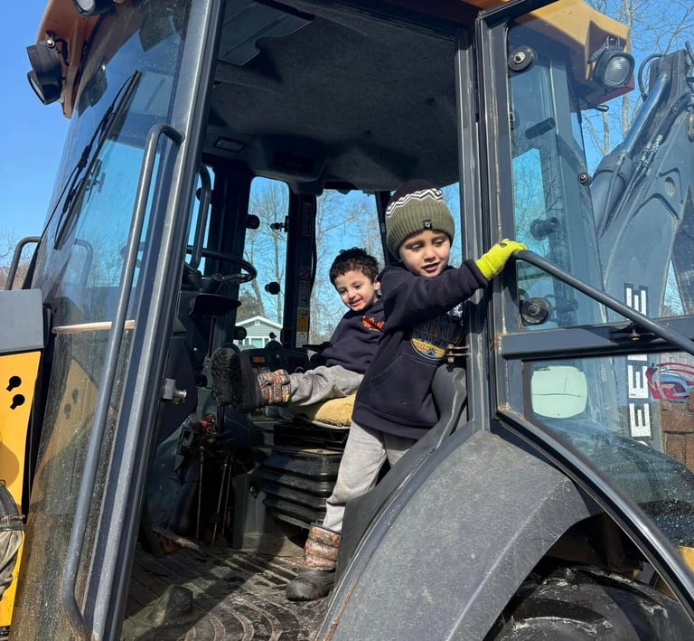 Two young boys playing inside the driver's cab of a yellow John Deere construction tractor.