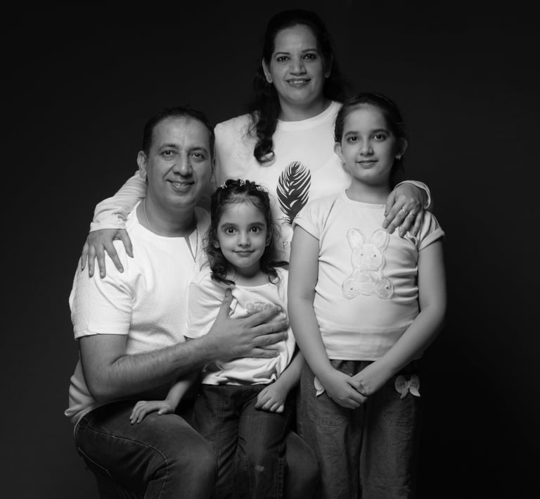 Black and white studio portrait of a smiling Indian family of four posing against a dark background.