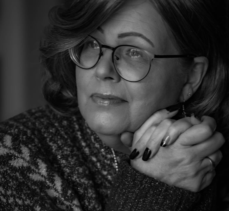 Black and white portrait of a woman with glasses and manicured nails wearing a patterned sweater.