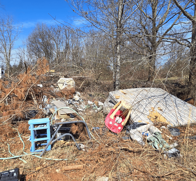 Image of a yard full of debris and trash, old mattresses, car toy, plastic shelf, yard debris.