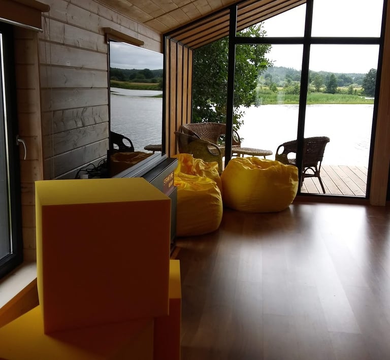 Modern log cabin interior featuring yellow bean bags and floor-to-ceiling windows overlooking a scenic lake.