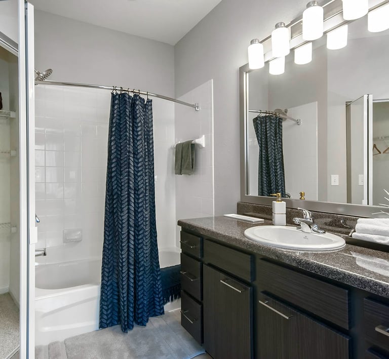 Modern bathroom featuring a dark wood vanity, granite countertop, and a shower with a blue patterned curtain.