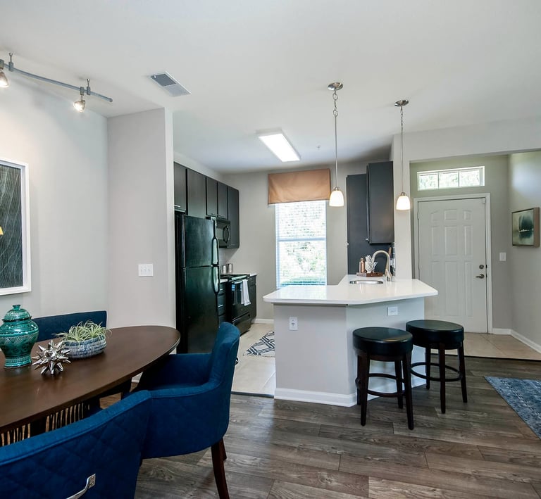 Modern open concept apartment interior featuring a dark wood dining table, blue chairs, and a kitchen with white counters.