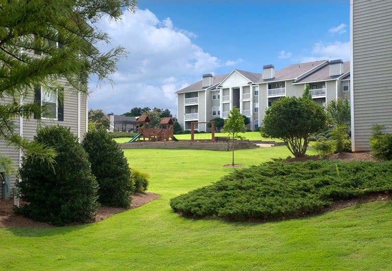Suburban apartment complex featuring a wooden children's playground on a lush green lawn.