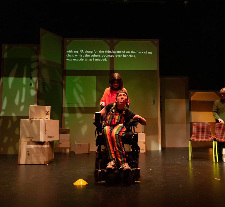 A white electric wheelchair user with a white person balanced on the back, and a BSL interpreter