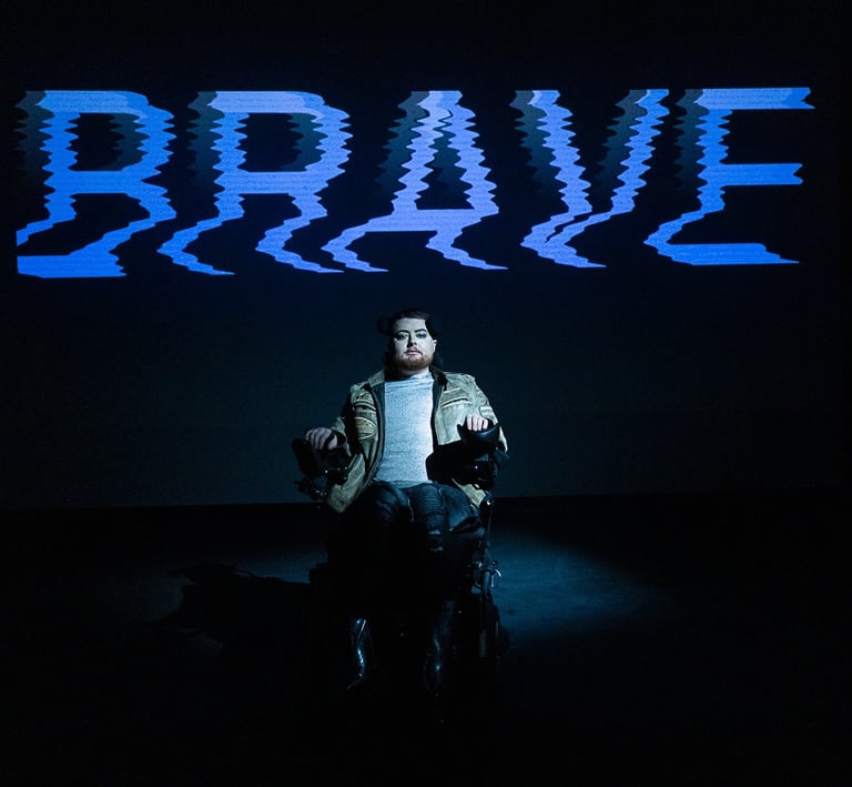 A white electric wheelchair user in a leather jacket in front of the word BRAVE