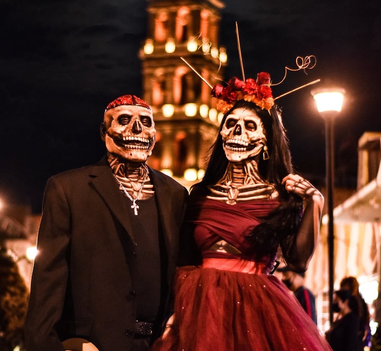 Couple in skull masks celebrating Day of the Dead in front of a Mexican cathedral.