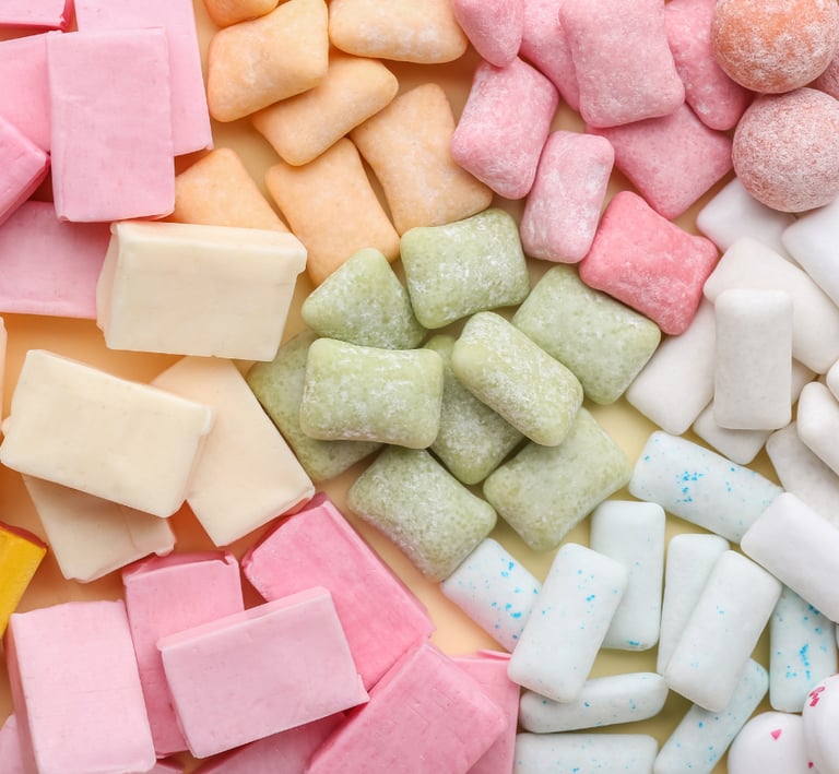 A colorful flat-lay assortment of rectangular and round chewing gum pieces in pink, green, yellow, and white.