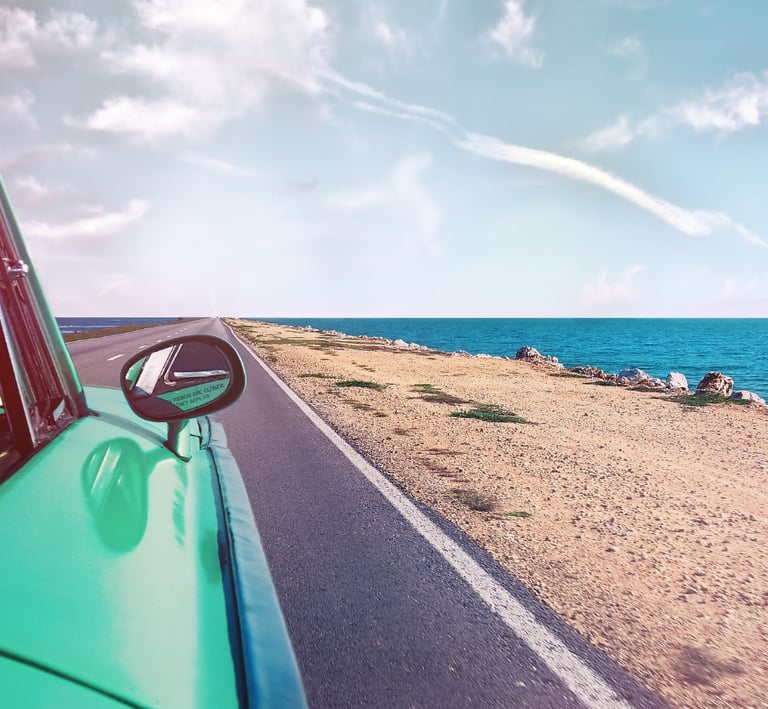 View looking down an open coastal highway and blue ocean from a vintage green car window.