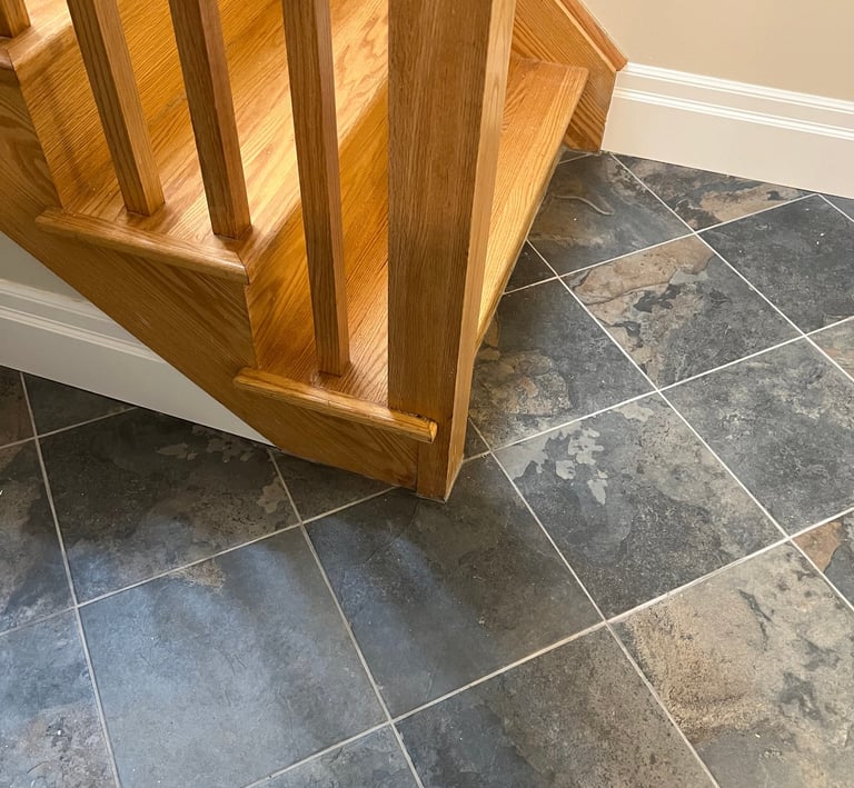 Natural oak wood staircase landing on a grey slate tile floor.