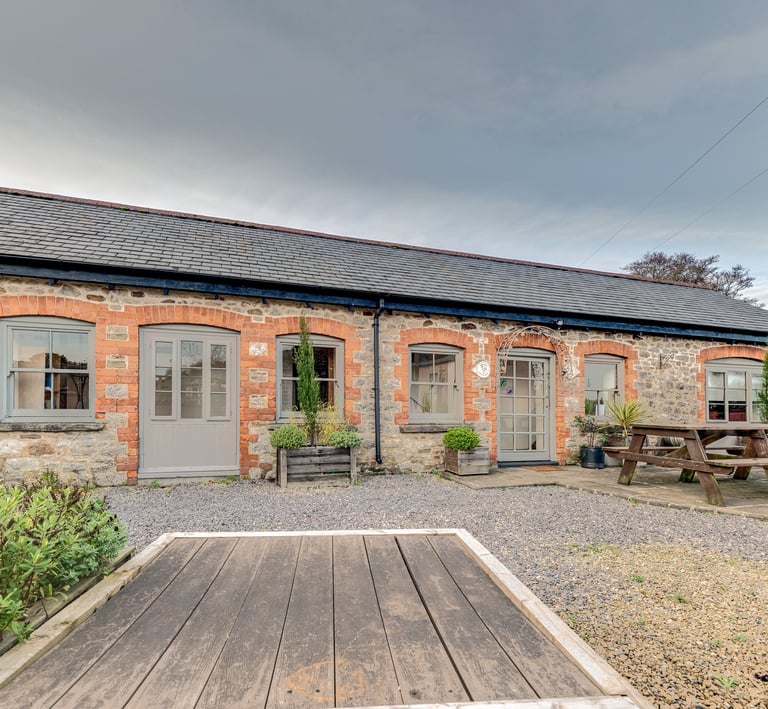 Stone cottage exterior with grey wooden doors and a rustic picnic bench on a gravel patio.