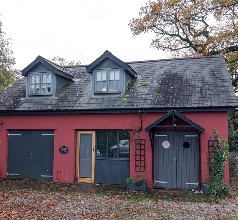 A charming red barn-style guesthouse with grey doors and dormer windows nestled among autumn trees.