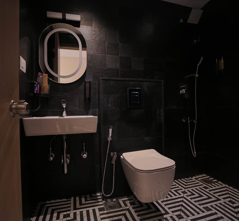 Modern luxury bathroom with black wall tiles, a white wall-hung toilet, and an illuminated mirror.