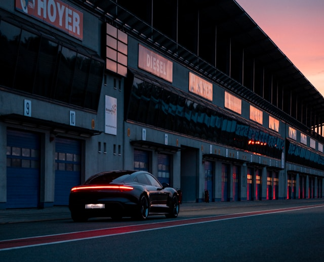Black Porsche Taycan electric car parked on a race track pit lane at sunset.