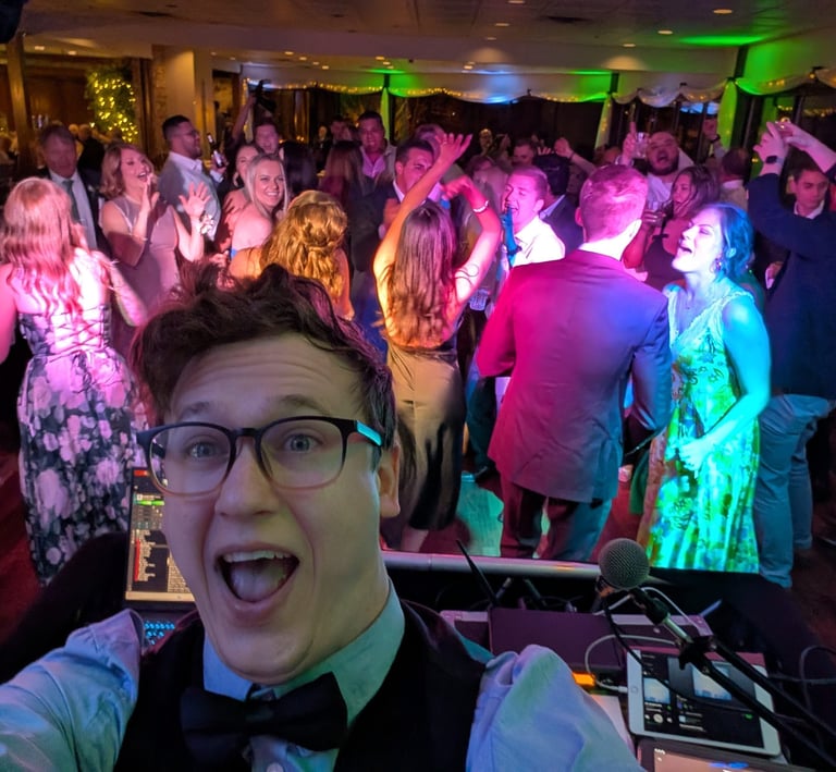 wedding DJ poses for a selfie in front of a packed dance floor
