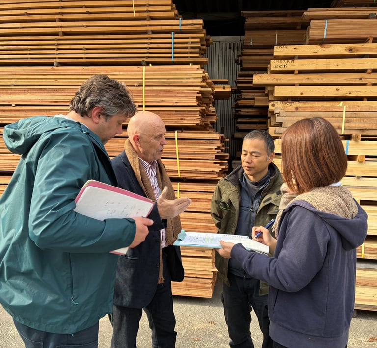 Four people discussing business while standing in front of stacked lumber at a wood processing yard.