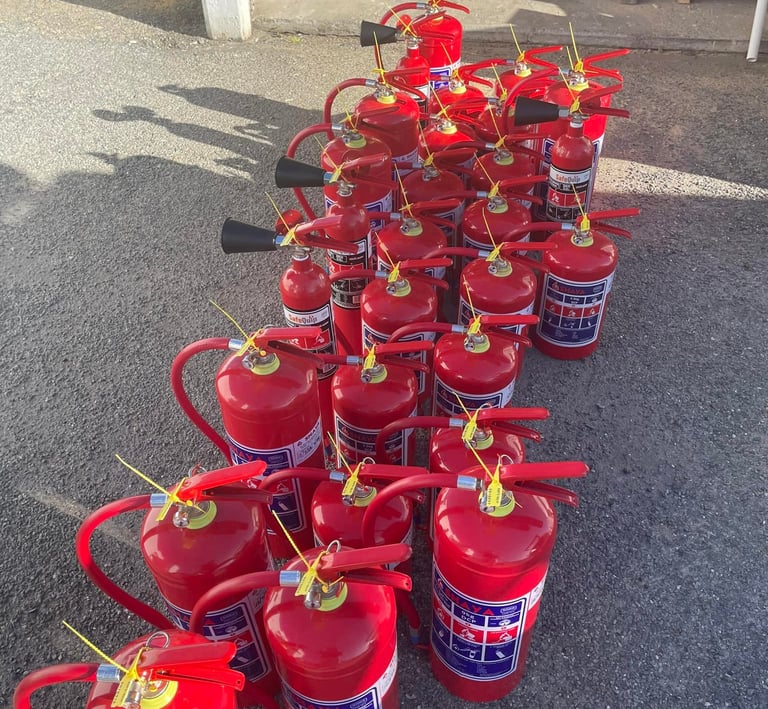 A collection of red portable fire extinguishers arranged on a pavement for inspection or safety maintenance.