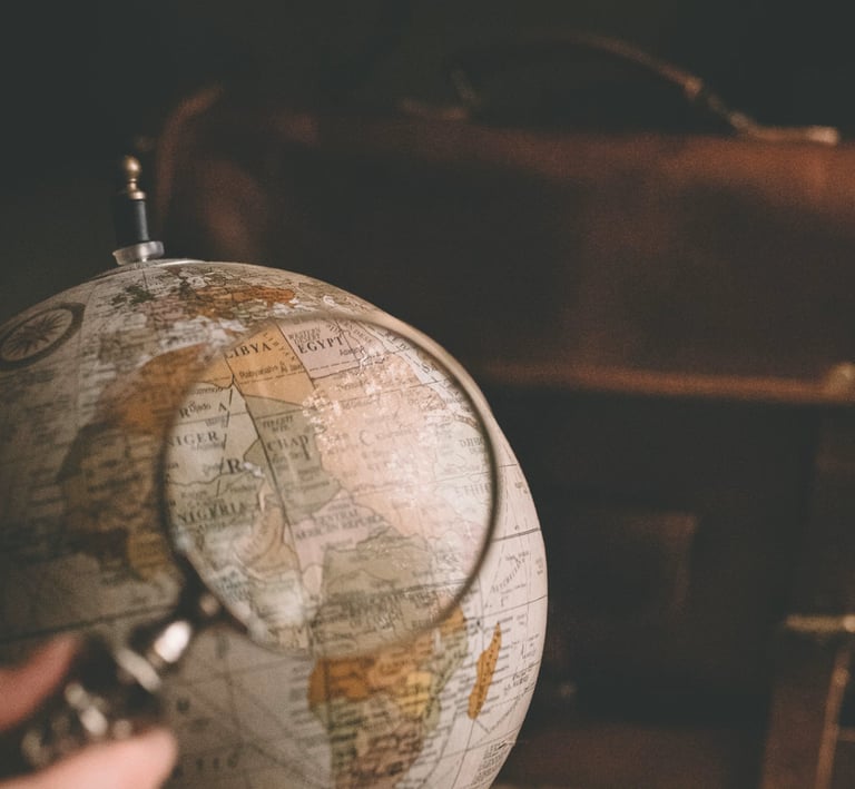 A magnifying glass held over a vintage world globe next to a leather travel bag for adventure planning.