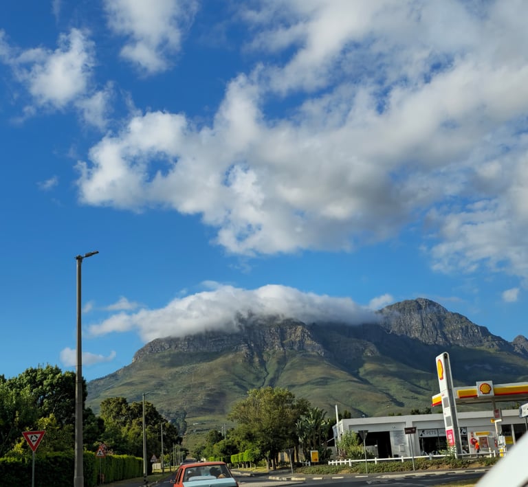A scenic view of a cloud-capped mountain peak behind a Shell gas station under a blue sky.