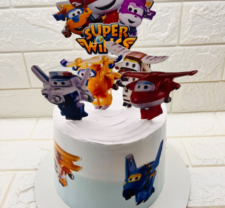 A Super Wings themed birthday cake with white frosting and airplane character cake toppers.
