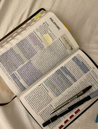An open bible with highlighted scriptures with pens on a white linen sheet.