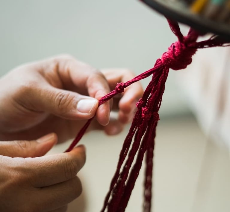 Manos tejiendo nudos para pieza de macramé en color rojo