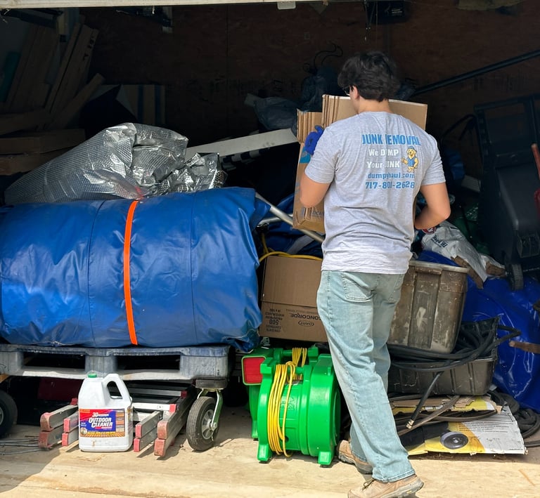 Professional junk removal worker clearing out a cluttered garage filled with boxes and debris.