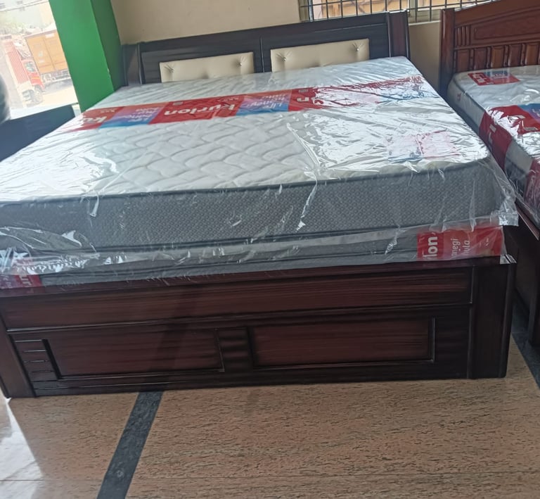 Modern dark wood double bed frame with a white quilted mattress wrapped in protective plastic.