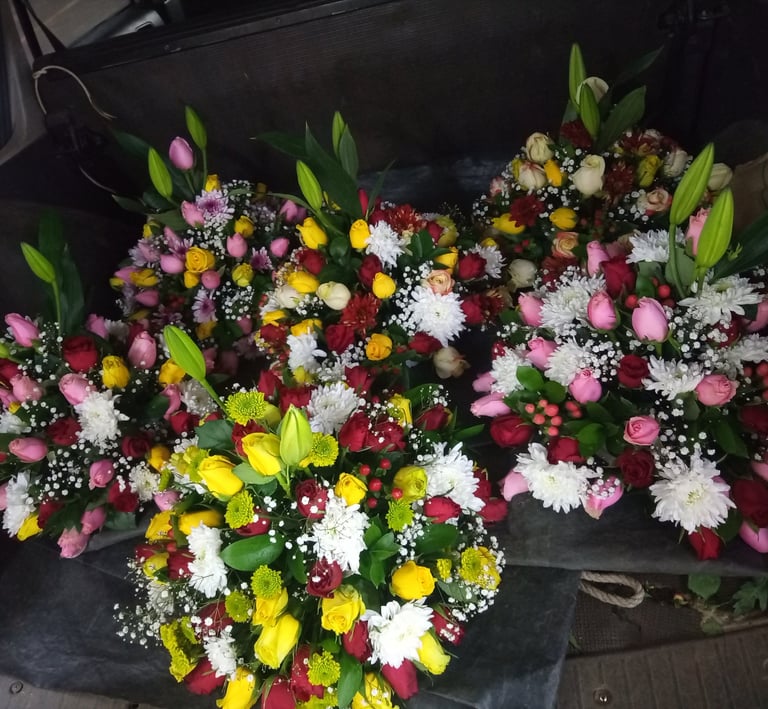 Assorted colorful flower bouquets with roses, lilies, and daisies in a car trunk for delivery.