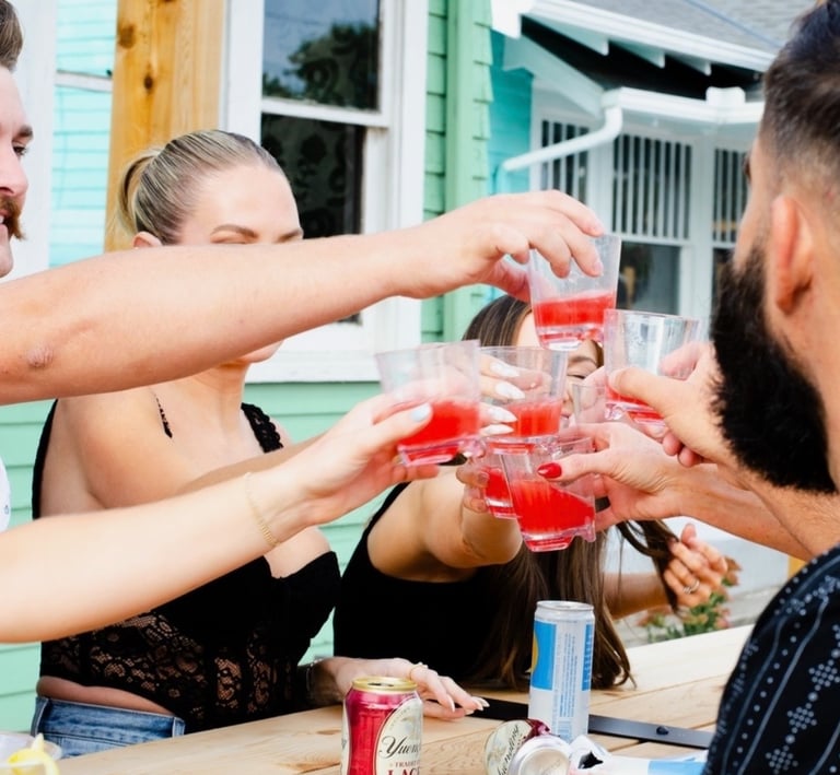 Group of friends cheering with red alcoholic shots at an outdoor patio bar.