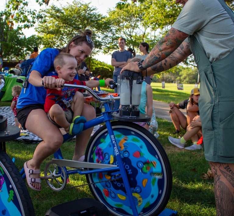 A little kid and a parent powering a smoothie on our blender bike