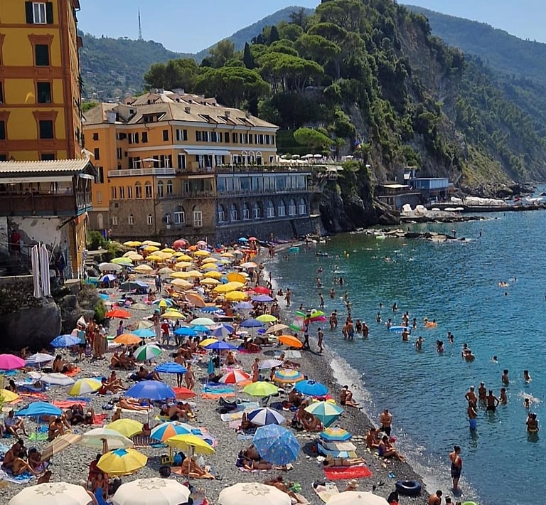 Crowded pebble beach with umbrellas in Camogli, Liguria Italy.