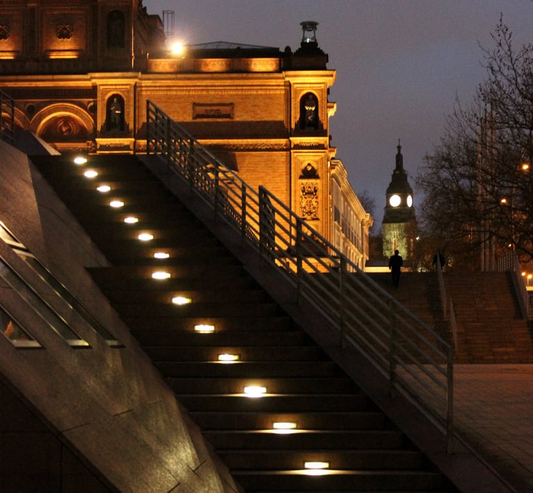 a lit staircase leading up to a building with a clock tower in the background