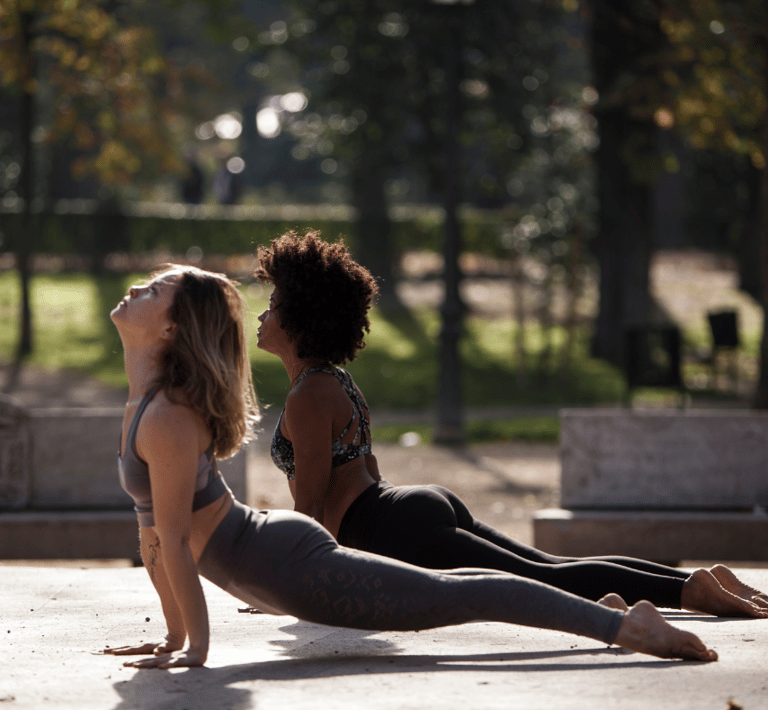 two women doing upward-facing dog yoga pose in a park