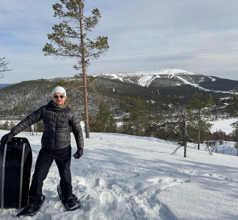 a man standing in the snow with a snowboard with a hill and beautiful snowy background
