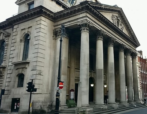 numerous columns  large church building with large door and an old clock in the middle 