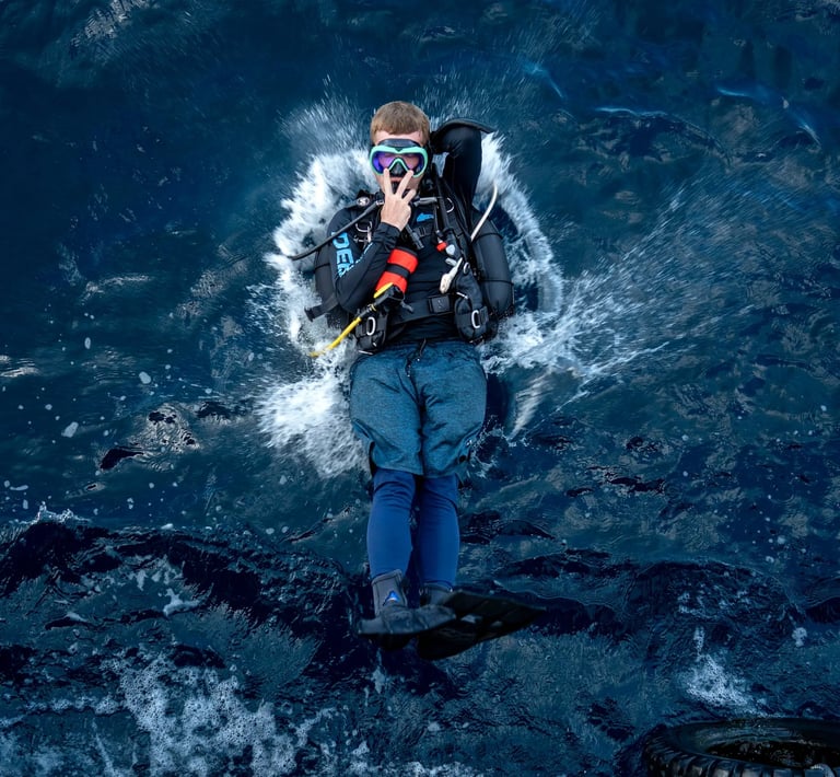 Scuba diver performing a back roll entry into deep blue ocean water from a dive boat.