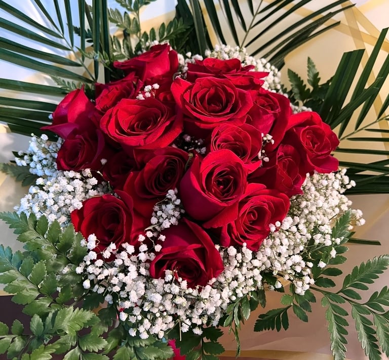 A bouquet of fresh red roses and white baby's breath flowers with green palm leaf accents.